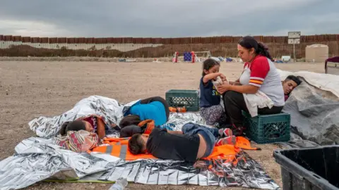 Getty Images Children sleeping on ground, mother sitting on milk crate while talking to daughter