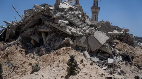 Reuters Israeli soldier sits next to a destroyed building in Rafah, in the southern Gaza Strip, during a tour for reporters (3 July 2024) 